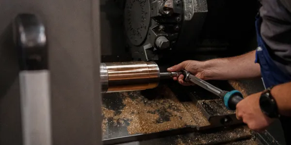 Ein Mitarbeiter bedient eine CNC-Drehmaschine und bearbeitet ein zylindrisches Metallstück, umgeben von Metallspänen.